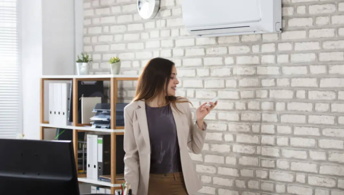 Air-Conditioning-and-Heating Nő az irodában fűtésre állítja a légkondícionáló berendezést